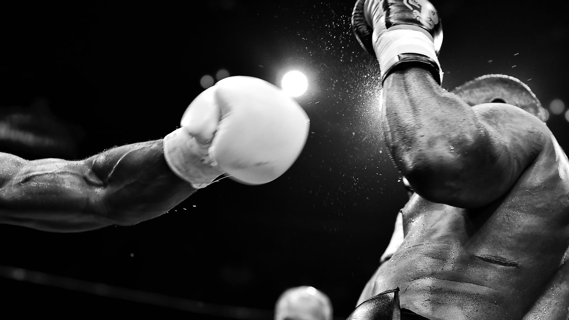 Zwei schwarze Boxer im Ring, der linke holt zum Schlag aus.
